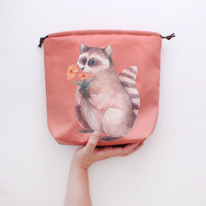 illustrated image of raccoon holding flowers on a project bag 