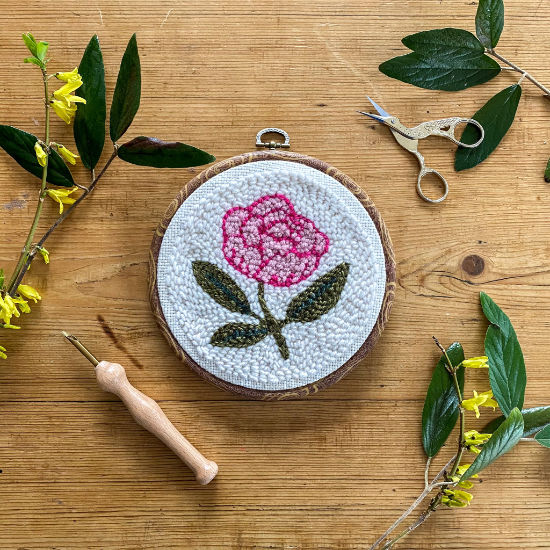 Pink peony punch needle kit completed with punch needle and scissors on a wood background