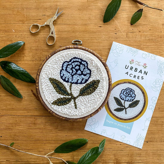 Completed blue peony punch needle kit with scissors on a wood background