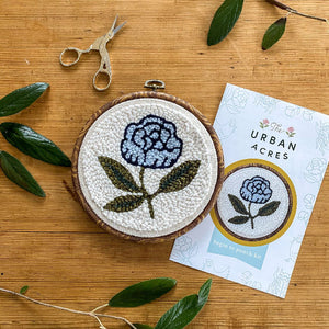 Completed blue peony punch needle kit with scissors on a wood background